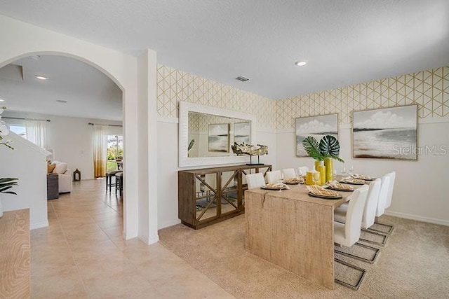 dining space featuring wallpapered walls, baseboards, arched walkways, an accent wall, and a textured ceiling