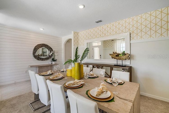 tiled dining space featuring carpet, visible vents, a textured ceiling, baseboards, and wallpapered walls