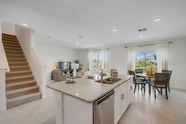 kitchen with light stone counters, visible vents, a kitchen island with sink, a sink, and dishwasher