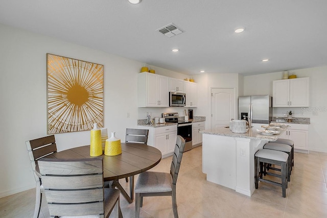 kitchen featuring a breakfast bar, a center island with sink, visible vents, appliances with stainless steel finishes, and white cabinetry