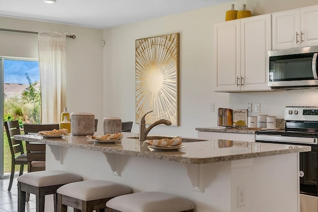 kitchen featuring light stone counters, appliances with stainless steel finishes, a sink, and a breakfast bar