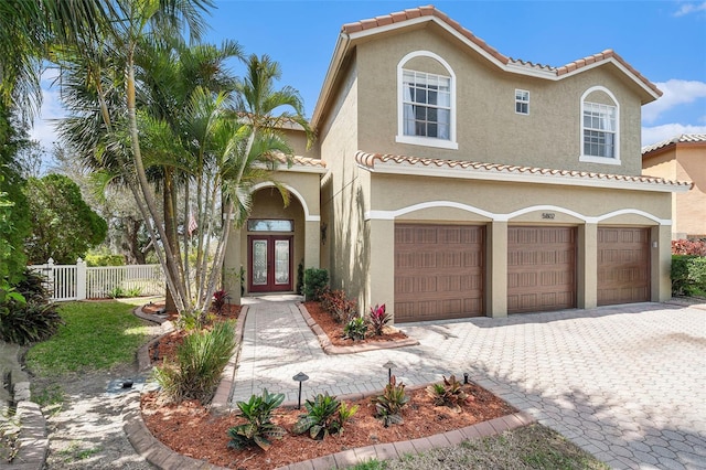 mediterranean / spanish-style home with decorative driveway, a tile roof, fence, and stucco siding