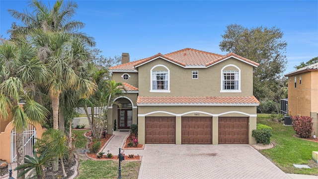 mediterranean / spanish home featuring decorative driveway, a chimney, a tile roof, and stucco siding