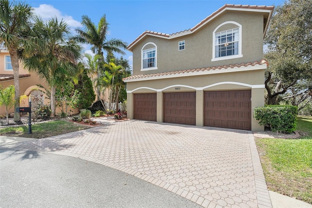 mediterranean / spanish home featuring a garage, a tiled roof, decorative driveway, and stucco siding