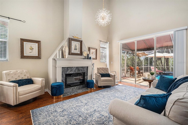 living area featuring a towering ceiling, wood finished floors, a high end fireplace, and a healthy amount of sunlight