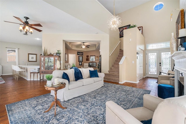 living area featuring stairs, ceiling fan with notable chandelier, wood finished floors, and baseboards