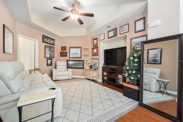 living room with baseboards, visible vents, a ceiling fan, wood finished floors, and a tray ceiling