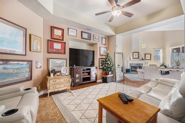 living room featuring visible vents, a high end fireplace, ceiling fan, wood finished floors, and baseboards