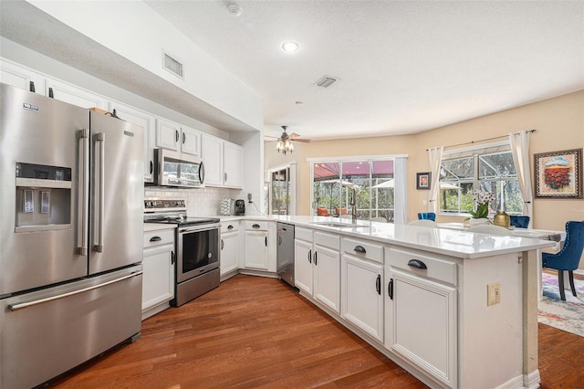 kitchen featuring visible vents, appliances with stainless steel finishes, a sink, wood finished floors, and a peninsula