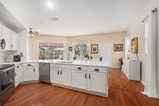 kitchen with stainless steel appliances, decorative backsplash, a sink, wood finished floors, and a peninsula