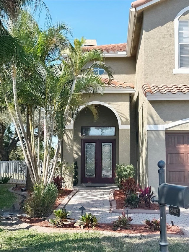 view of exterior entry with fence, a tiled roof, an attached garage, and stucco siding