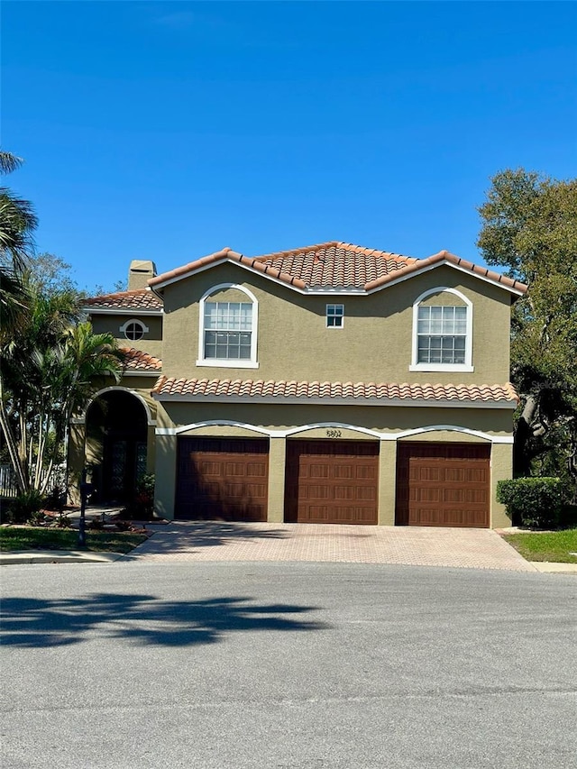 mediterranean / spanish-style house featuring decorative driveway, an attached garage, a tile roof, and stucco siding