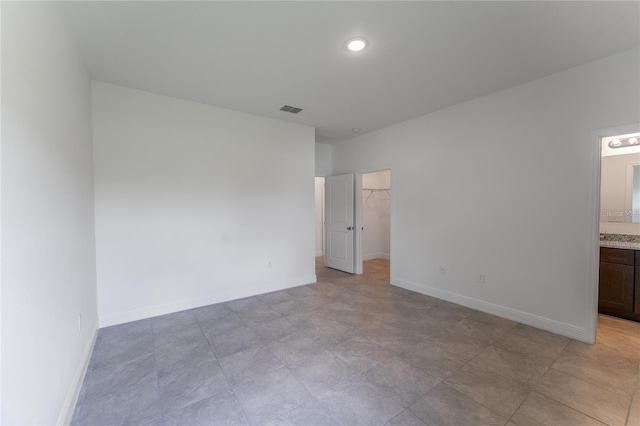 unfurnished bedroom featuring a walk in closet, a closet, visible vents, connected bathroom, and baseboards