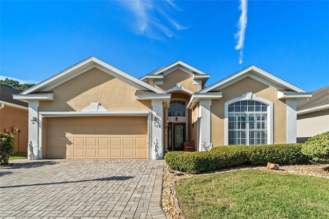 ranch-style home with an attached garage, decorative driveway, and stucco siding