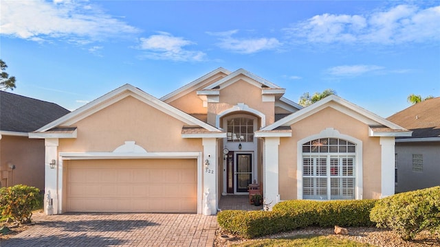 traditional-style house with a garage, decorative driveway, and stucco siding