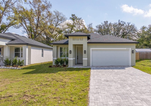 prairie-style home featuring a garage, fence, decorative driveway, a front yard, and stucco siding