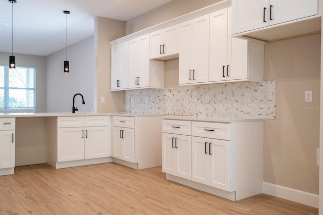 kitchen with hanging light fixtures, a sink, light wood-style floors, white cabinetry, and backsplash