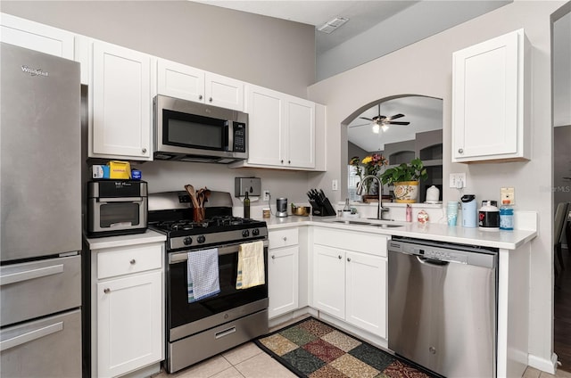 kitchen featuring arched walkways, white cabinets, appliances with stainless steel finishes, light countertops, and a sink