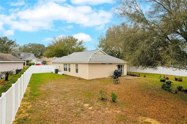 rear view of house with stucco siding, a fenced backyard, and a yard