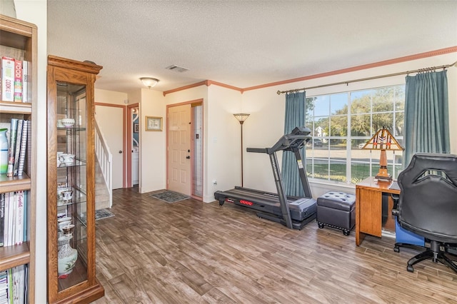 workout area with a textured ceiling, ornamental molding, wood finished floors, and visible vents