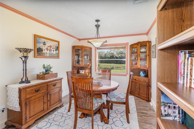 dining space with baseboards, visible vents, ornamental molding, a textured ceiling, and light wood-style floors