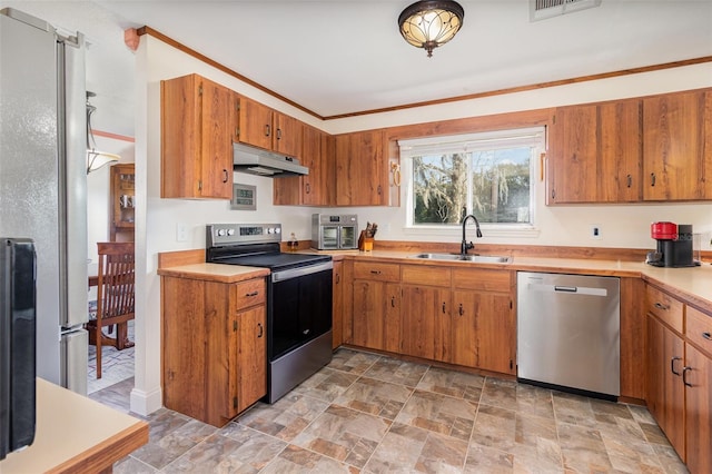 kitchen featuring under cabinet range hood, a sink, light countertops, appliances with stainless steel finishes, and brown cabinetry