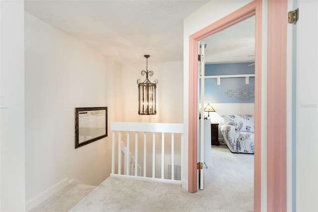 hallway with visible vents, an upstairs landing, a textured ceiling, carpet flooring, and a chandelier