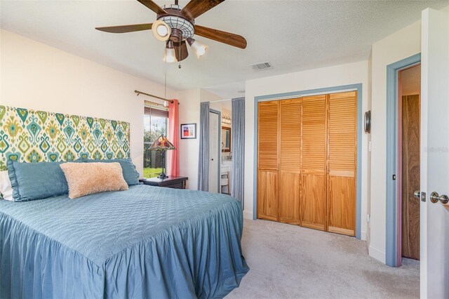 bedroom with a textured ceiling, carpet floors, visible vents, a ceiling fan, and two closets