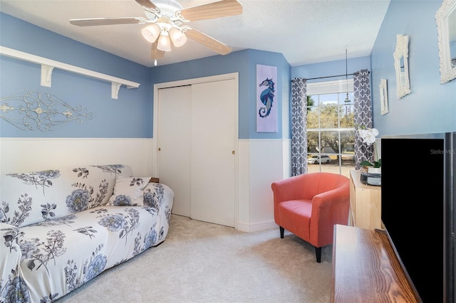 carpeted living room featuring wainscoting, ceiling fan, and a textured ceiling