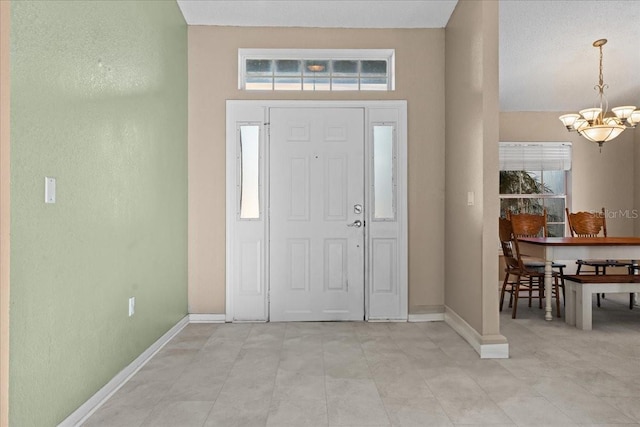 entrance foyer with an inviting chandelier, light tile patterned flooring, and baseboards