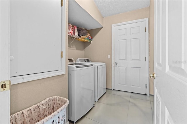 clothes washing area featuring light tile patterned floors, a textured ceiling, washing machine and dryer, and laundry area