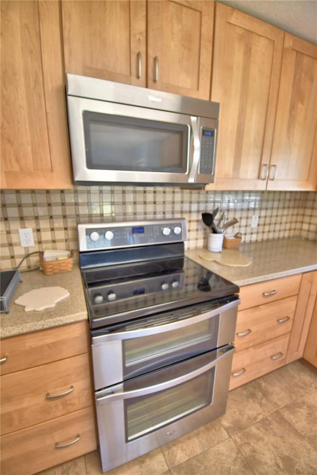 kitchen with decorative backsplash, light tile patterned floors, light stone countertops, and stainless steel appliances