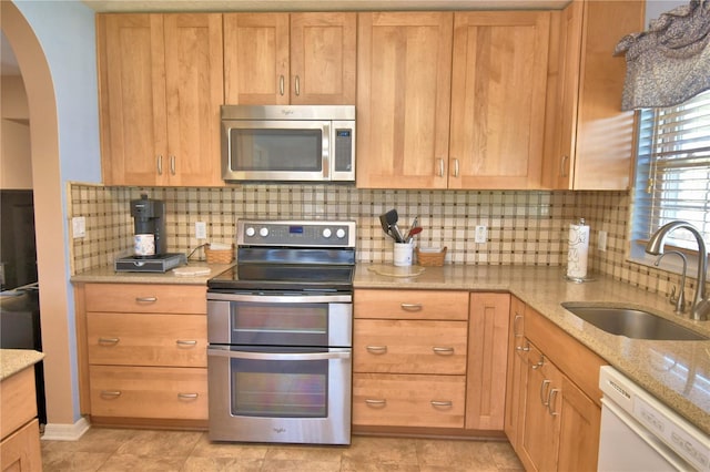 kitchen featuring tasteful backsplash, light stone counters, appliances with stainless steel finishes, arched walkways, and a sink