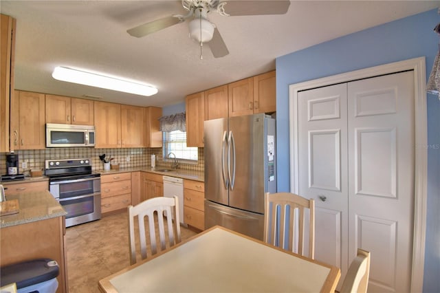 kitchen featuring backsplash, light brown cabinetry, stainless steel appliances, a ceiling fan, and a sink