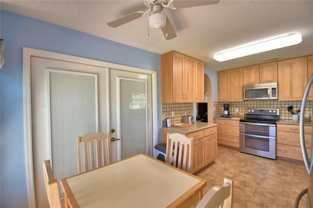 kitchen featuring arched walkways, light brown cabinetry, light countertops, appliances with stainless steel finishes, and backsplash