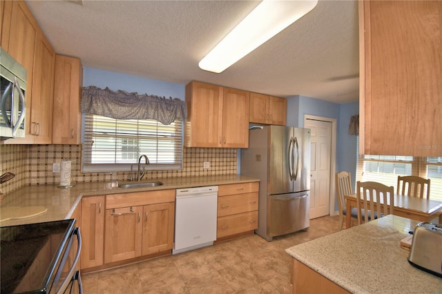 kitchen with light brown cabinets, a sink, appliances with stainless steel finishes, a textured ceiling, and backsplash