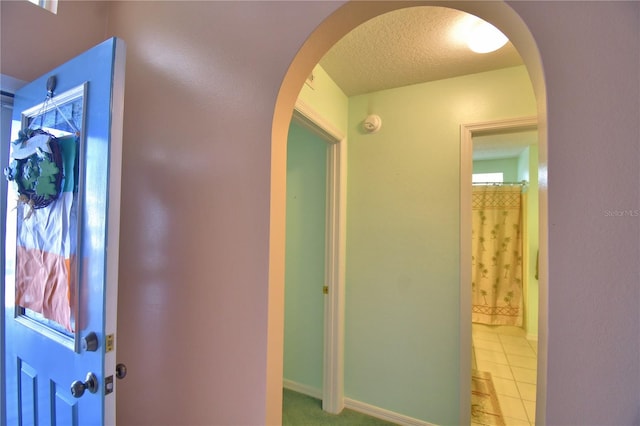 entrance foyer with arched walkways, light tile patterned floors, a textured ceiling, and baseboards