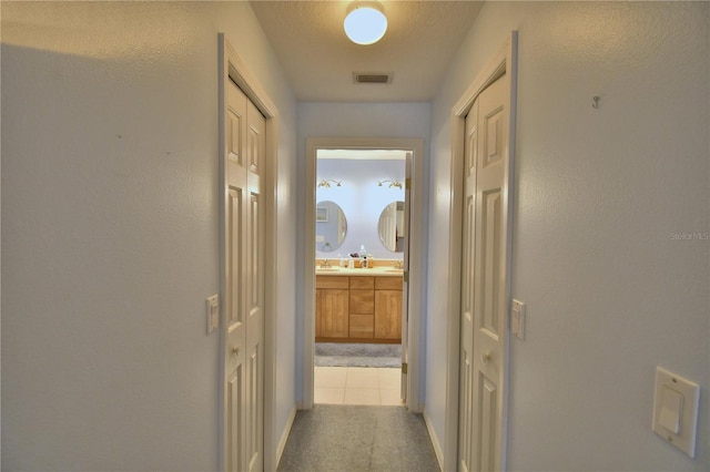 hallway featuring visible vents, carpet, and a sink