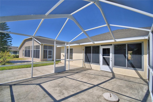 back of property featuring glass enclosure, a patio area, roof with shingles, and stucco siding