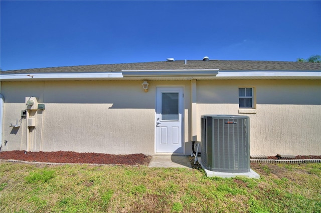 entrance to property featuring a shingled roof, cooling unit, and stucco siding