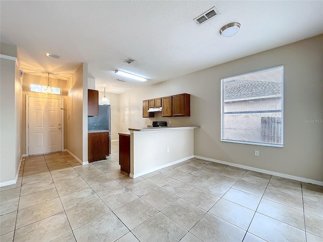 kitchen featuring brown cabinets, light tile patterned floors, visible vents, a peninsula, and under cabinet range hood