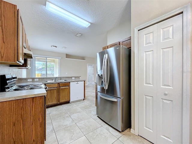 kitchen featuring light tile patterned flooring, electric range, stainless steel refrigerator with ice dispenser, dishwasher, and brown cabinetry