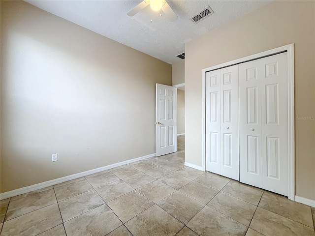 unfurnished bedroom featuring a textured ceiling, light tile patterned flooring, visible vents, baseboards, and a closet