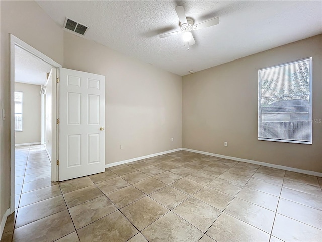 unfurnished room featuring visible vents, ceiling fan, a textured ceiling, and light tile patterned floors