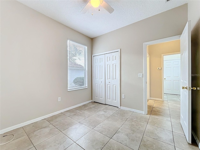 unfurnished bedroom featuring light tile patterned floors, a closet, ceiling fan, a textured ceiling, and baseboards