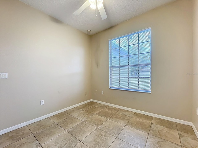 empty room featuring a textured ceiling, light tile patterned floors, a ceiling fan, and baseboards