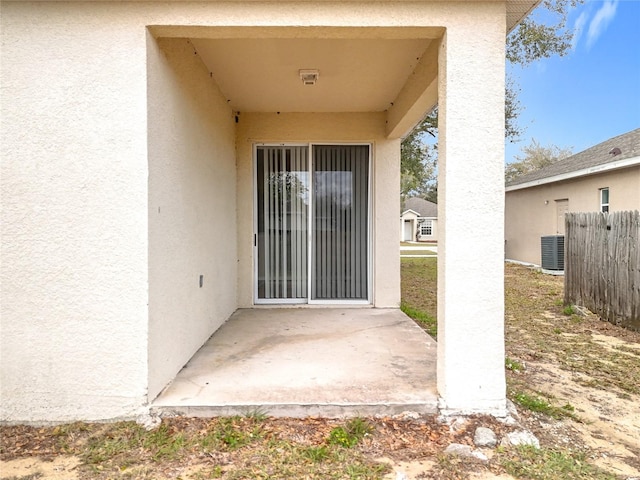 doorway to property featuring a patio, central AC, fence, and stucco siding