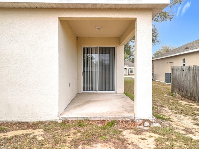 view of exterior entry with a patio area, fence, and stucco siding