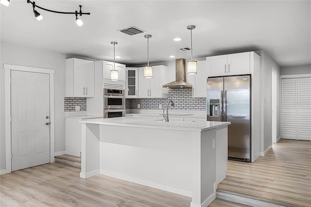 kitchen featuring visible vents, light countertops, wall chimney range hood, and appliances with stainless steel finishes