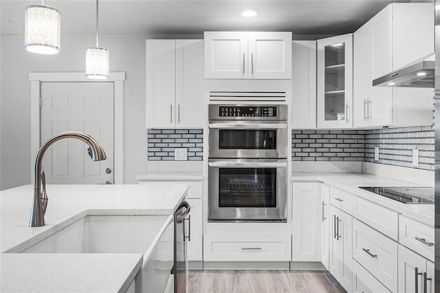 kitchen with tasteful backsplash, white cabinets, black electric cooktop, stainless steel double oven, and a sink